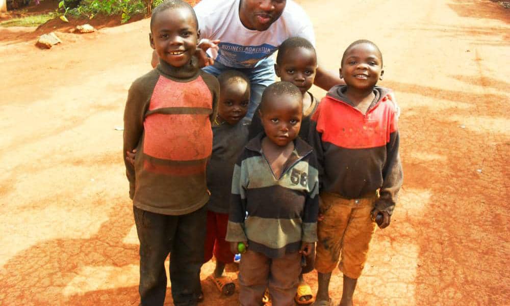 A group of young children on a red earth road with an NISD volunteer crouching behind them.