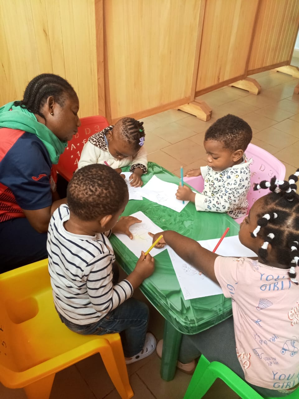 A teacher seated with four small children drawing at a low table.